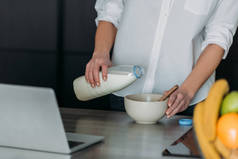 在厨房笔记本电脑旁，一位妇女正在往碗里倒牛奶
