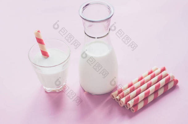 粉红色背景上的一瓶牛奶和一杯牛奶。