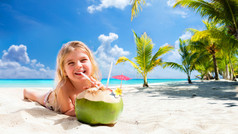 在热带海滩喝椰子鸡尾酒的小女孩