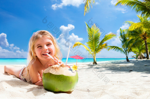 在热带海滩喝椰子鸡尾酒的小女孩