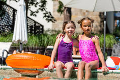 穿着泳衣的女孩们坐在泳池边的充气球和吊环旁拥抱