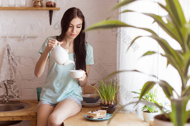 漂亮的黑发女人坐在厨房的桌子上，喝茶，吃华夫饼，甜点