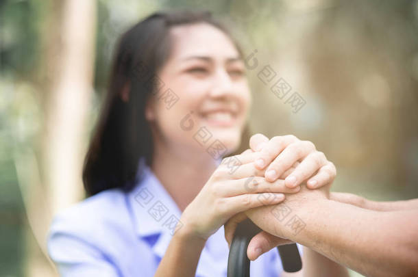 安慰的手。在户外花园里，年轻的护士牵着老人的手坐在长凳上。老年护理，