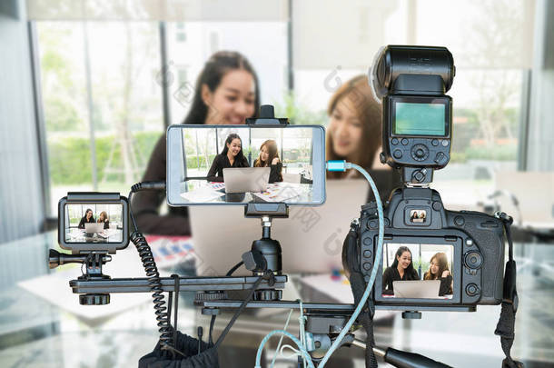 两名亚洲女青年通过Live stream 、 Live Streaming为创业者提供的概念接受采访时，在三脚架上装有智能手机和动作片的专业相机