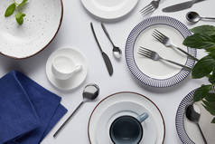 绿色的叶子, 不同的陶瓷板材, 杯子, 厨房毛巾, 叉子, 勺子和刀子在白色桌的上部看法 