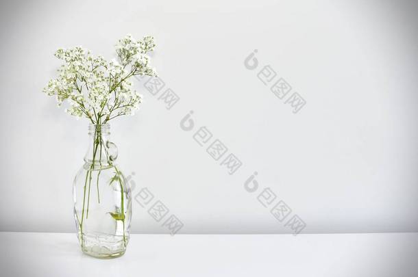 简洁简朴的构图，白色桌子上有白色花朵的玻璃瓶，文字空间.