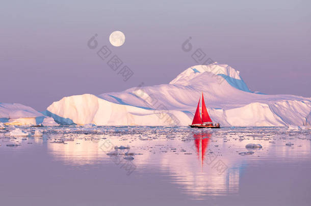 在极地夏季的午夜太阳季节, 小<strong>红帆船</strong>在迪斯科湾冰川的漂浮冰山之间游弋。伊卢利萨特, 格陵兰.