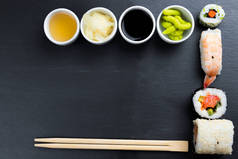 典型的亚洲菜设置在黑色厨房板上.生姜、日本辣椒酱、芥末、酱油和鱼露在小白碗里.筷子。Sushi - futomaki和nigiri 。帧中的复制空间.