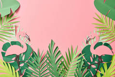 在粉红色背景的绿棕榈叶上剪纸火烈鸟的顶视图，带有复制空间