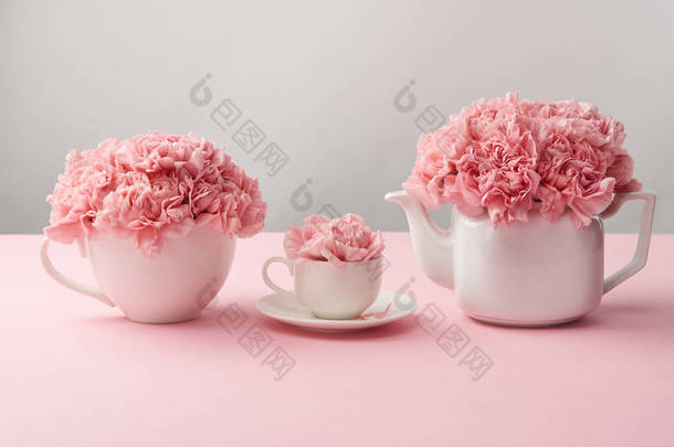 白色杯子和水壶与美丽的粉红色的花朵在灰色