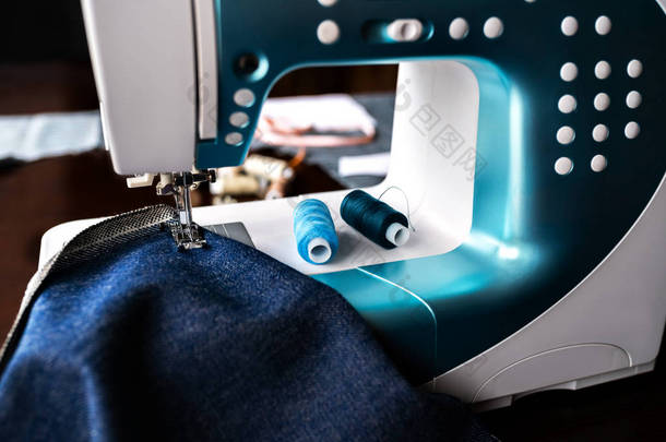 缝纫机与牛仔布和线缝纫，特写。带蓝布的缝纫机的一部分.