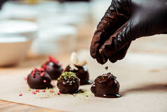 用黑色乳胶手套在新制作的糖果上加巧克力屑的巧克力粉的剪影 