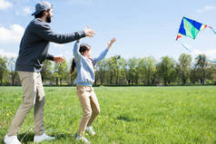 女儿和父亲的侧面飞行风筝在草甸 