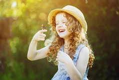 笑着的卷发女孩，手上拿着一只蝴蝶。快乐的孩子