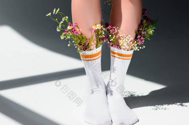 女孩与美丽的花朵在袜子站在灰色镜头 