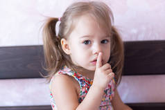 3岁的小女孩静静地坐在床上，摆出一个手指的姿势