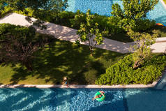 在蓝色的游泳池和绿色的花园，只有一个在阳光下躺在扁平的气球上的女人的头像照片.