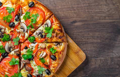 切片披萨与莫扎雷拉奶酪，番茄，胡椒，橄榄，蘑菇，香料和新鲜叶。木制餐桌上的意大利披萨
