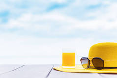 海滩上有鲜橙汁的黄色帽子.蓝天背景空间的暑假.