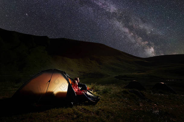 男人和女人在晚上休息, 在 Dogyaska 湖附近的喀尔巴阡山山露营, 坐在帐篷里, 看着布满星星的天空。在帐篷灯上.