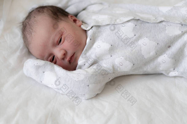 刚出生的婴儿在出生的头几分钟睁大眼睛躺在背上。一个<strong>新生</strong>的、带有原始油脂痕迹的婴儿斜视着他的眼睛。宝宝看起来像在眯着眼.