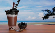可可豆珍珠奶茶，将黑色珍珠或泡沫果冻放在透明的玻璃杯中，将棕色的稻草放在木制桌子上，模糊了大海和海滩的景色。3D渲染.