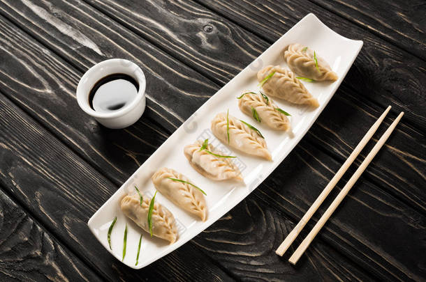 筷子旁边的盘子里放着美味的中国水饺，黑木桌上放着酱油