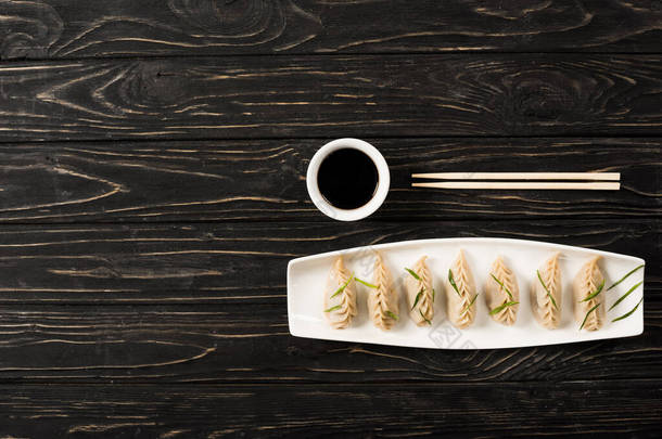 <strong>筷子</strong>附近盘子里美味的中国水饺和黑树林里的酱油俯视图