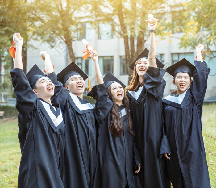 大学校园里穿着毕业礼服拿着毕业证书的快乐学生