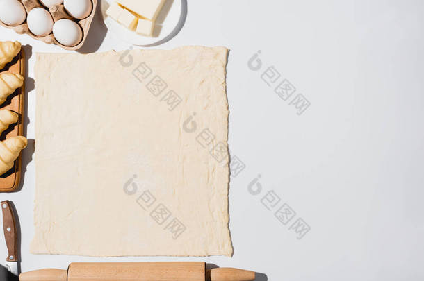 生面团、刀片、滚针、黄油和白底鸡蛋附近木制切菜板上新鲜羊角面包的顶部视图