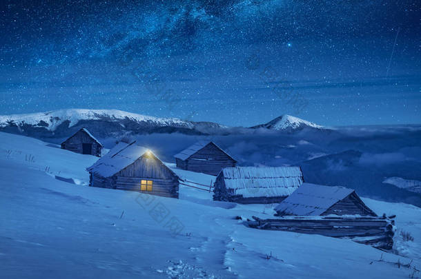 喀尔巴阡山脉的村庄由月光照亮, 山上的木制房屋覆盖着新鲜的积雪。梦幻般的银河在星空下。冬夜<strong>圣诞节</strong>.