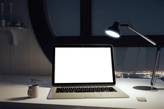 桌子上的空白白色笔记本电脑屏幕和办公室的灯