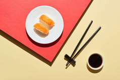 在酱油旁边放上鲑鱼，红色和米黄色表面放上筷子的新鲜黑鬼的头像