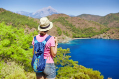 带背包的年轻女子旅行者站在悬崖边上, 望着地中海的风景, 夏日度假的概念