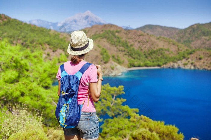 带背包的年轻女子旅行者站在悬崖边上, 望着地中海的风景, 夏日度假的概念