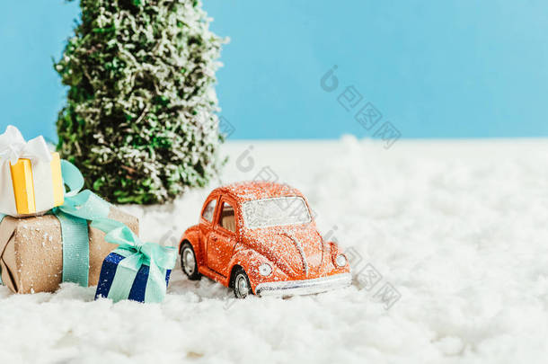 玩具车的特写镜头与礼物<strong>和</strong>圣诞树站立在由棉花制成的雪在蓝色背景
