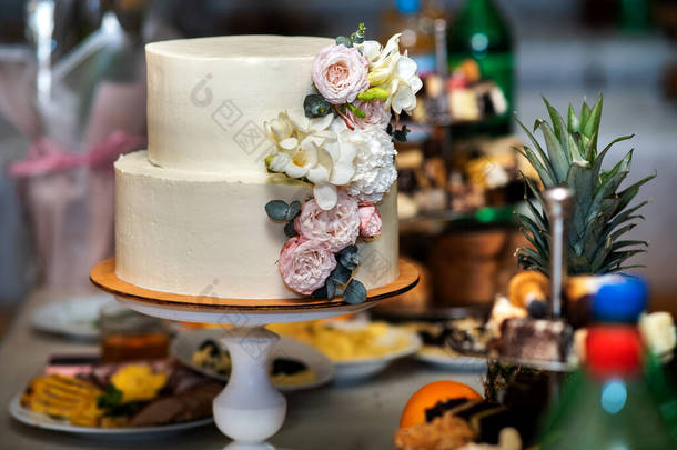 高高的甜婚礼蛋糕，桌上装饰着鲜活的粉色和白色花朵.