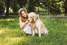 白色连衣裙和草帽美丽的女孩在草地上坐在草地上看着狗的全长视图