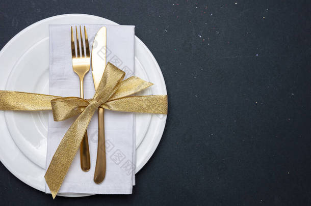 白色盘子上的金色餐具，黑色背景，顶视图