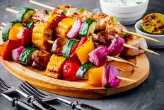 烤菜鸡串配甜玉米、辣椒粉、西葫芦、洋葱、西红柿和蘑菇在木盘子上