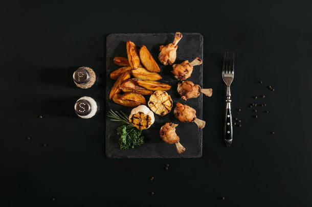 在黑色石板板上的美味烤土豆鸡肉和烤大蒜的顶级视图 
