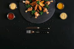 美味的烤土豆与炸鸡, 各种调味汁和叉子用刀在黑色的顶级视图