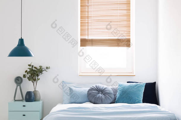 灯以上蓝色橱柜与植物旁边的床在<strong>简单</strong>的卧室内部与窗口。真实<strong>照片</strong>