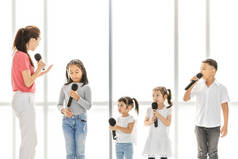 亚洲老师教亚洲孩子唱歌, 孩子们注意听她说话, 他们站在白色的大窗户前。音乐学校或歌唱课堂训练的概念.