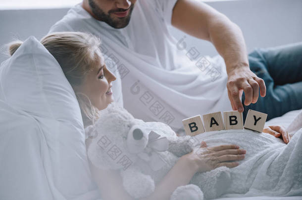 男子在怀<strong>孕</strong>的妻子与泰迪熊在家里的人把木块与婴儿字体的裁剪拍摄