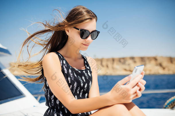 年轻女子乘坐智能手机在游艇上旅行。在游艇上聊天智能手机.