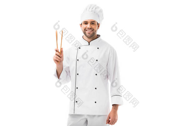 快乐的年轻厨师与木钳看相机孤立在白色