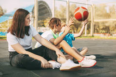 快乐的高中生坐在篮球场上，赛后放松，谈笑风生。体育、游戏和教育。友谊的概念