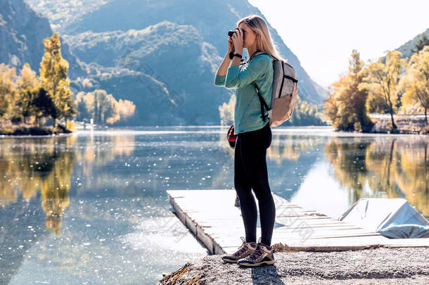 漂亮的年轻女子背着背包旅行，带着相机在湖中拍照.