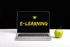 新鲜的绿色苹果和笔记本电脑在桌子上与电子学习字母和明星在屏幕上隔离在黑色